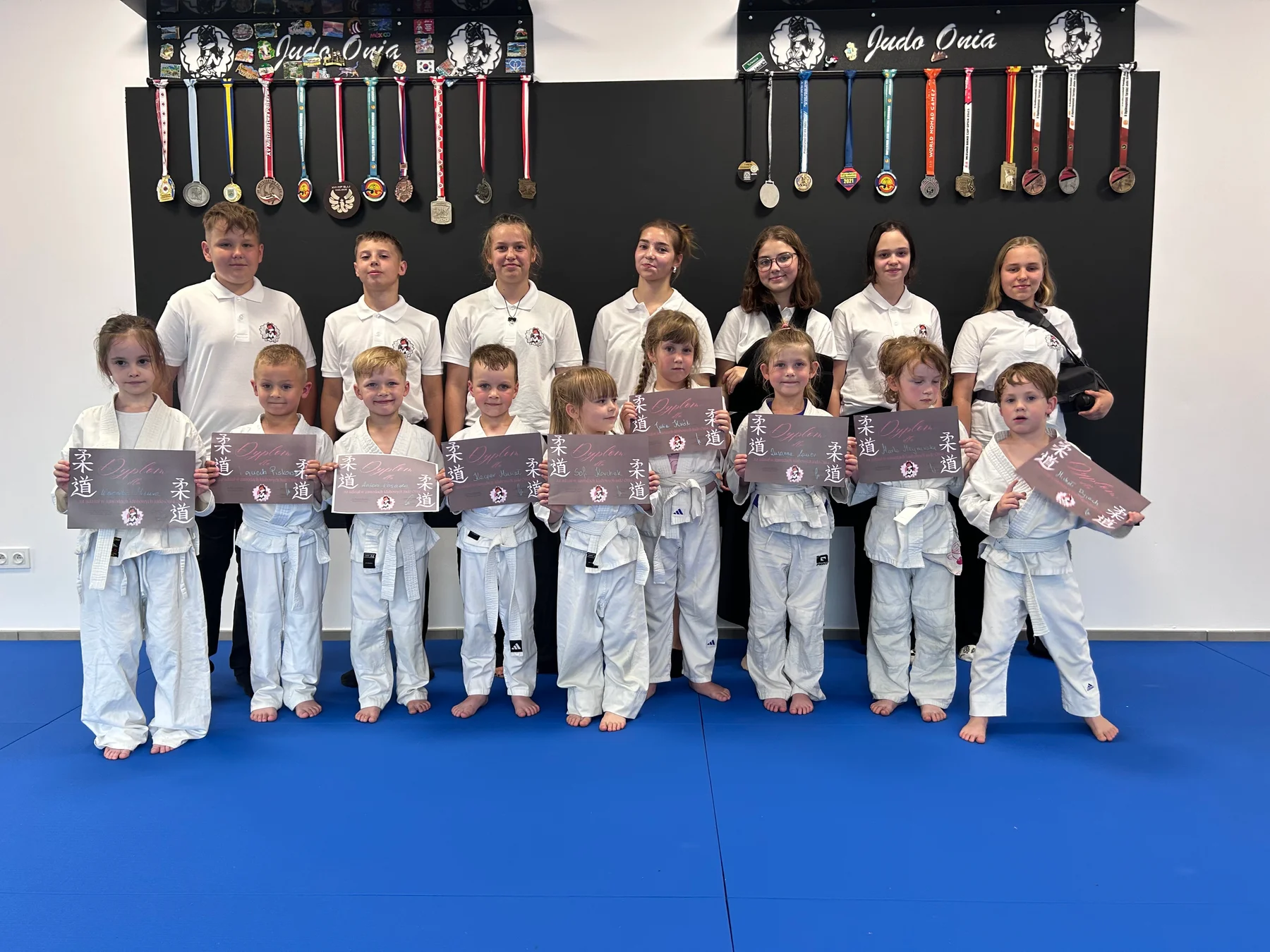 Dzieci w judogach z dyplomami i klubowa drużyna Judo Onia na tle medali